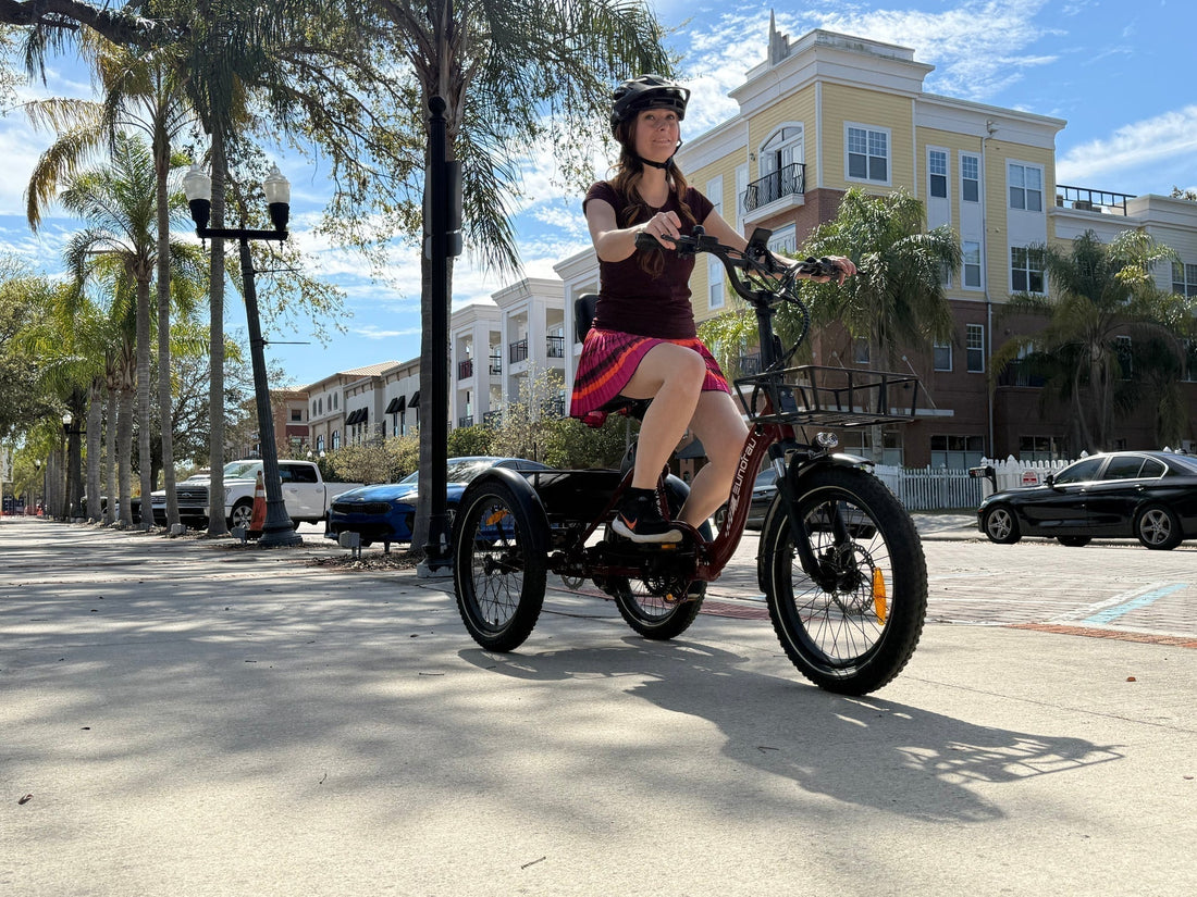Person riding a tricycle on a sidewalk with palm trees and buildings in the background.