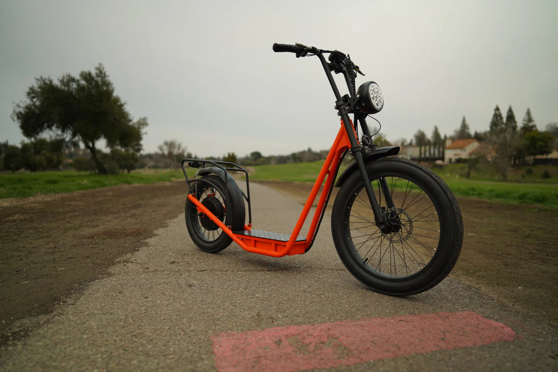 Orange electric scooter on a paved road with a rural landscape in the background.